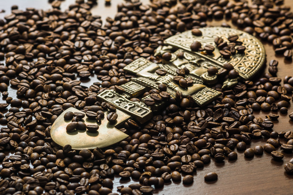Coffee spills out of the bag onto a dark wood table covering a Peruvian god statuette.
