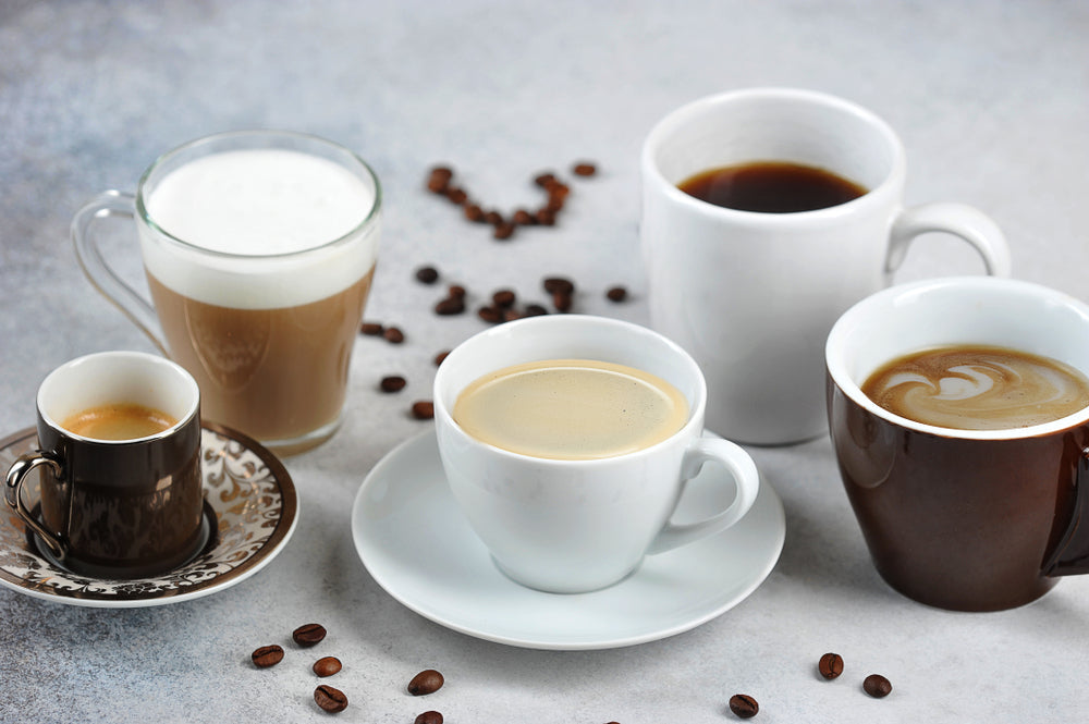 Different coffee drink types in different cups. Espresso, cappuccino, Americano, latte are presented. Coffee beans on the surface of a light table.