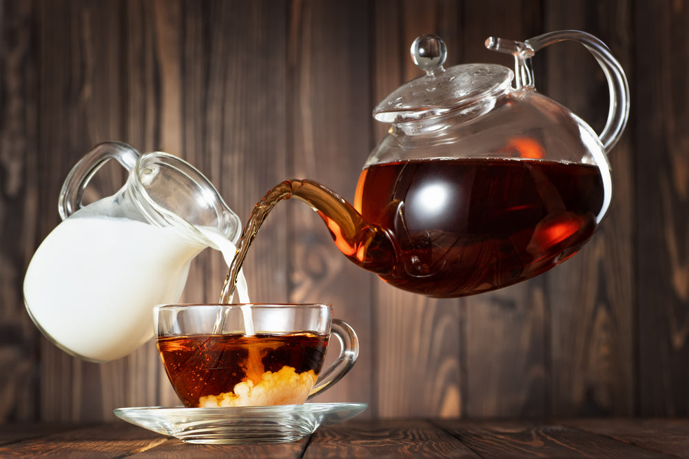 Flying teapot and jug pouring tea with milk into cup on wooden table.