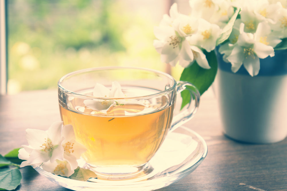Glass cup of jasmine tea with blooming jasmine branch in blue ceramic cup on wooden table.