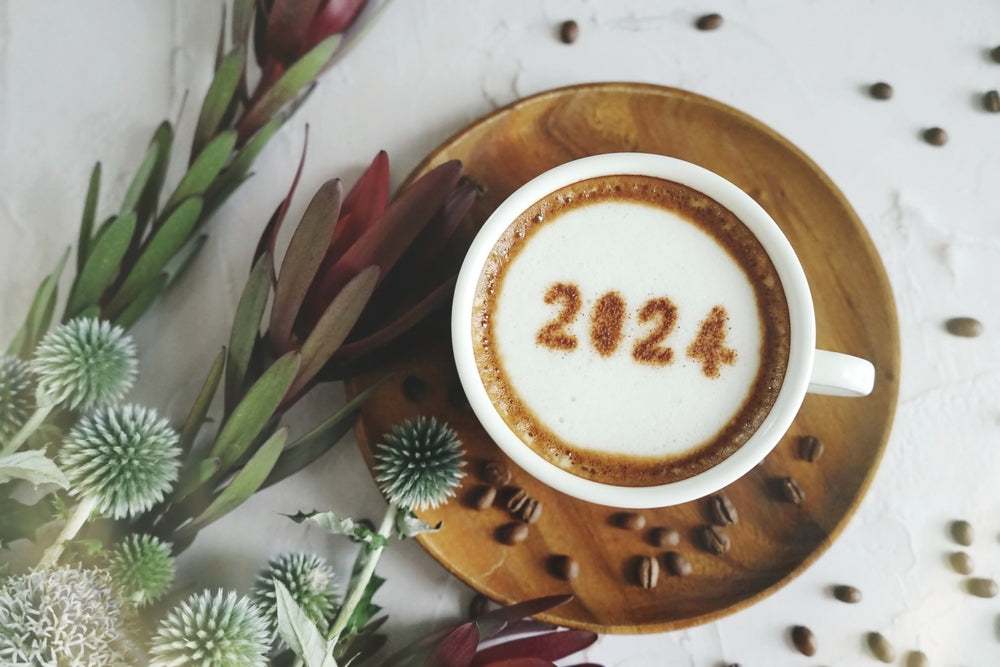 Happy New Year 2024 theme coffee cup with number 2024 over frothy surface served on wooden saucer and white cement background with coffee beans.