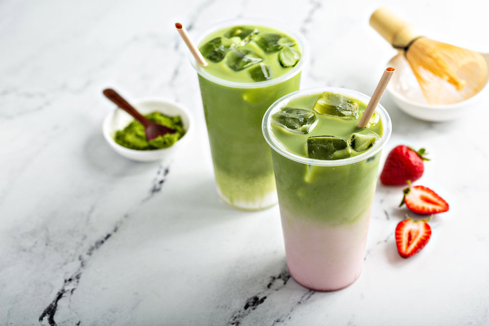 Two cold matcha lattes in a tall glasses with strawberry puree on marble background.