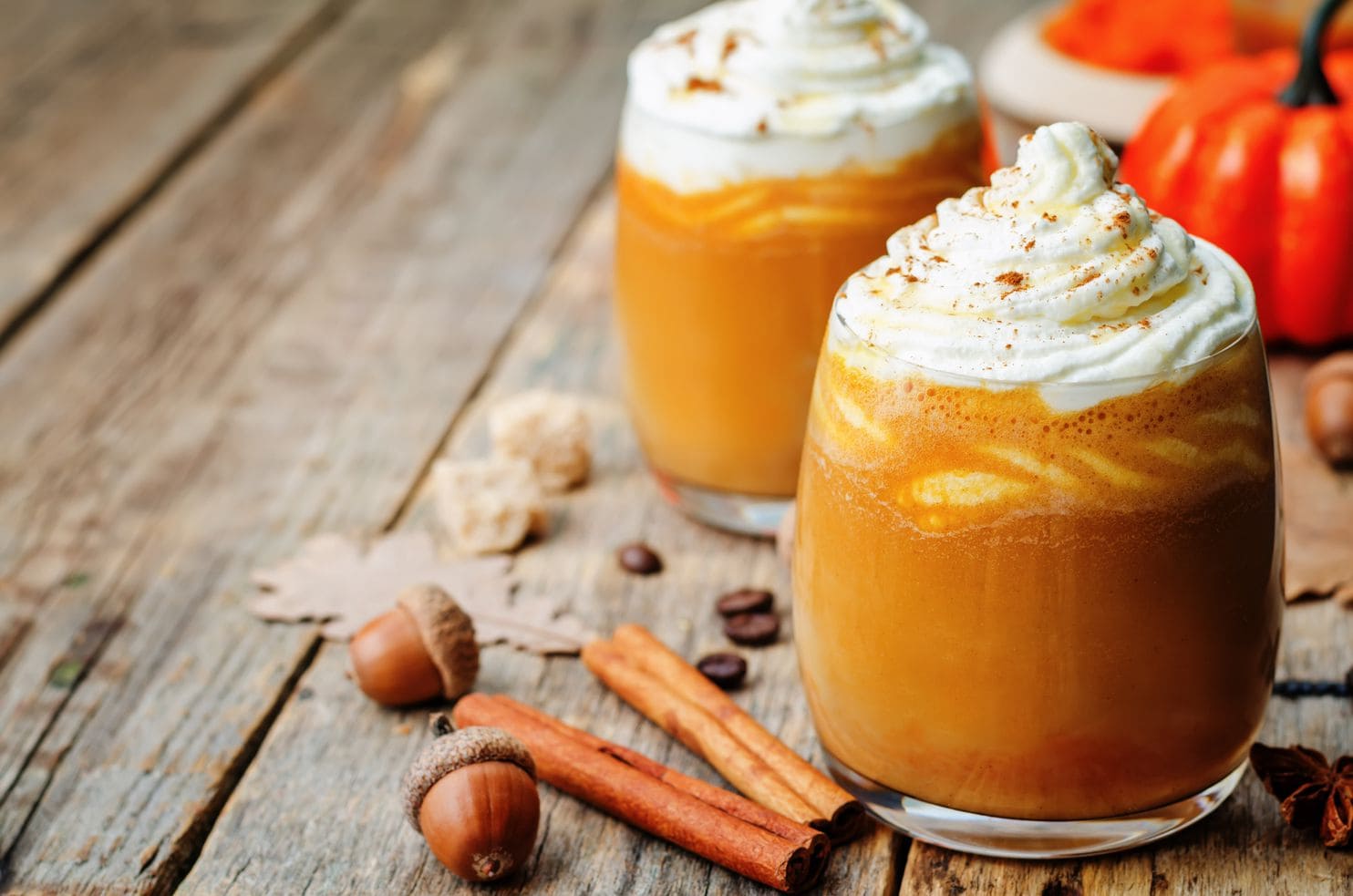 Two Pumpkin Spice Lattes in glasses with whipped cream toppings on a wooden table.